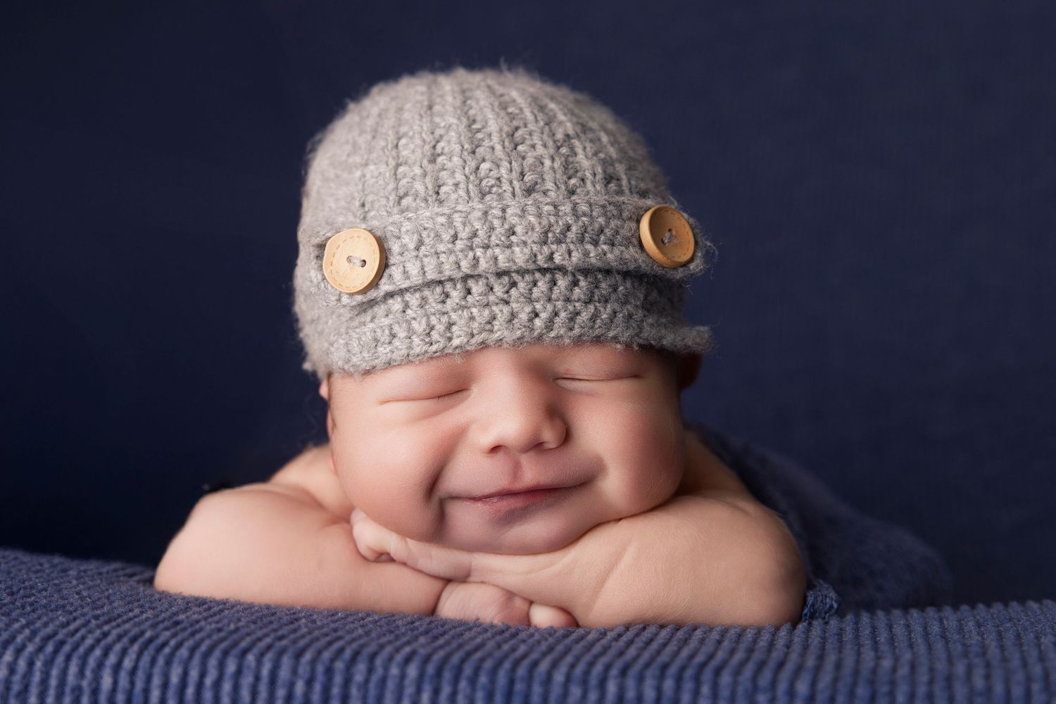 Baby wearing knit newsboy cap smiles while resting on blue blanket.