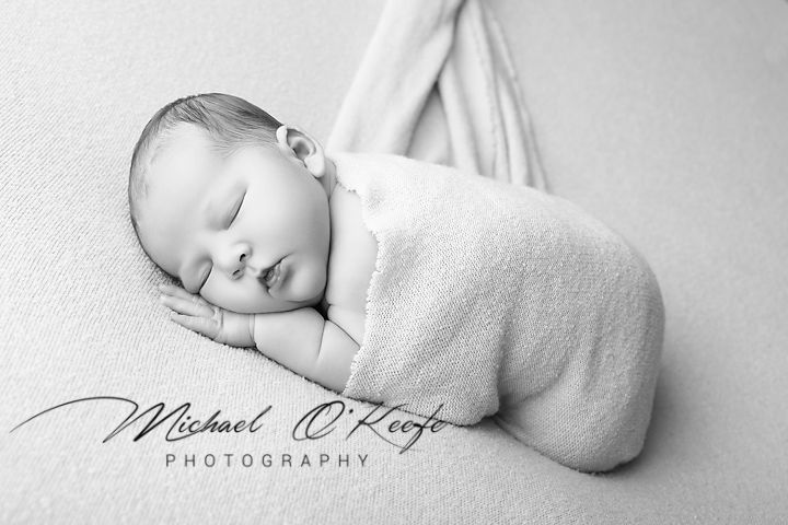 Black and white artistic newborn photography series showing peaceful sleeping baby wrapped in soft white blanket.