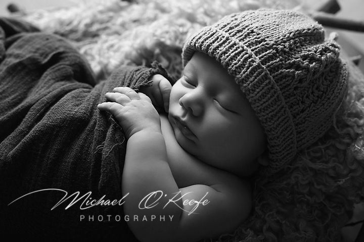 A series of seven black and white newborn photography portraits showing a sleeping baby wearing a knit hat.