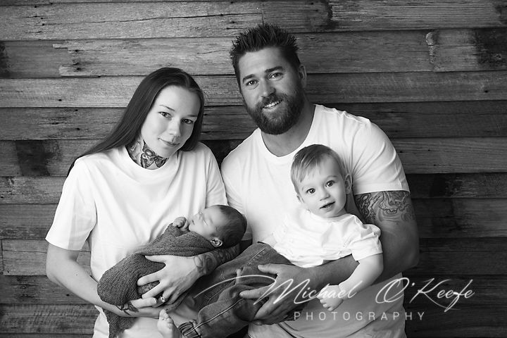 A series of black and white family photos showing playful moments against a rustic wooden wall backdrop.