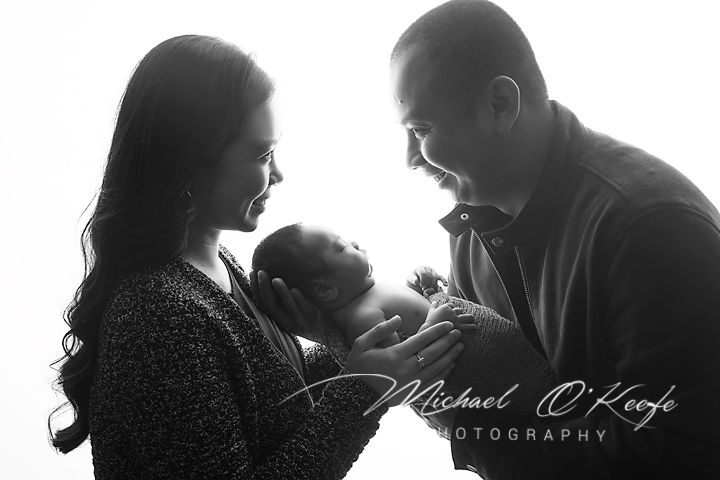 Black and white newborn photo of parents lovingly gazing at their baby, captured by Michael O'Keeffe Photography.