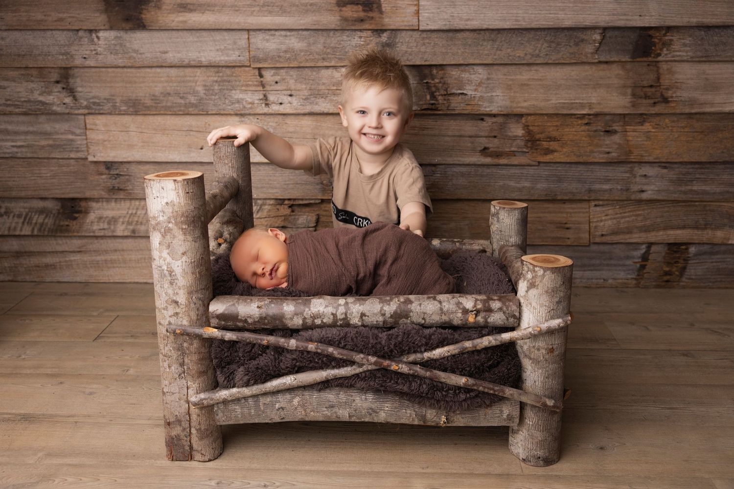 Small child sits happily on rustic log bench against wooden wall backdrop.