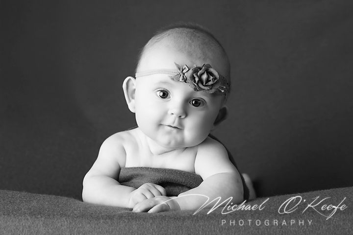 Black and white portrait of a baby wearing a delicate floral headband against a dark background.