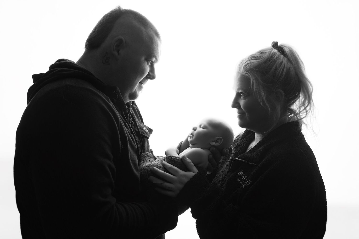 Black and white photo of parents holding their newborn baby, a tender family portrait in silhouette.