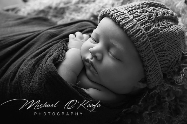 A peaceful sleeping baby wearing a knitted gray hat nestled in soft black fabric.