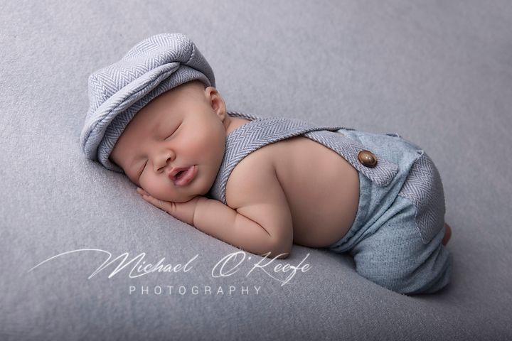 Sleeping newborn baby in gray knit wrap and hat lying on soft gray blanket during professional photography session.