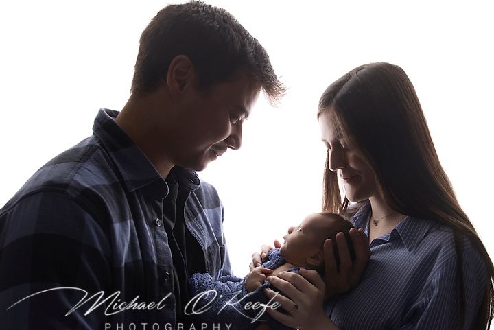 New parents lovingly gaze at their newborn baby in a bright studio portrait by Michael O'Keefe Photography.