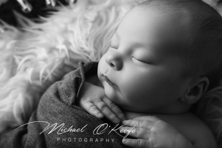 Black and white newborn portrait of a sleeping baby wrapped in soft blanket by Michael O'Keefe Photography.