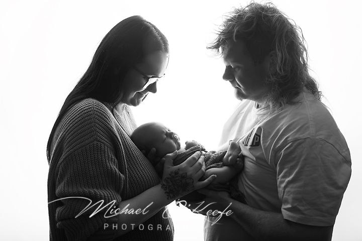 Black and white photo of two parents lovingly cradling their newborn baby, captured by Michael McLeefe Photography.