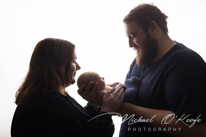 New parents tenderly hold their newborn baby in a beautiful backlit silhouette portrait by Michael O'Keefe Photography.