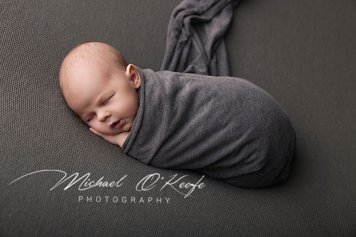 Newborn baby swaddled in a gray wrap sleeping peacefully on a gray background, professional newborn photography.