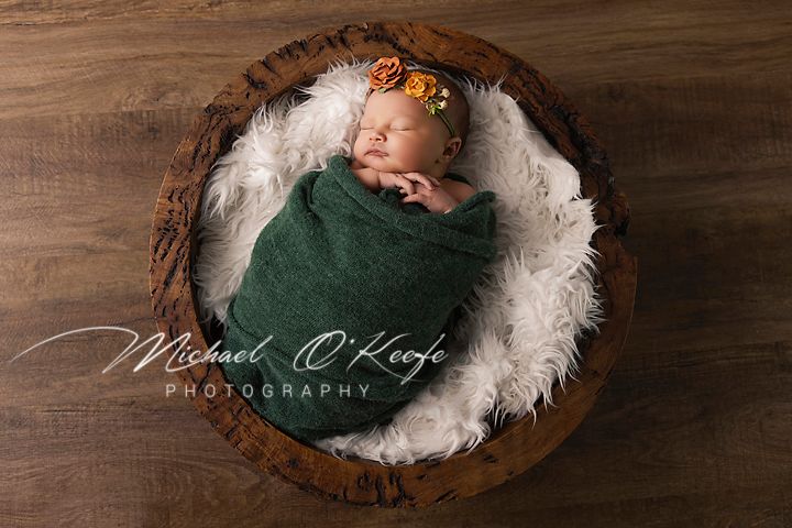 A newborn baby sleeps peacefully in a rustic wooden bowl lined with white feathers and soft textures.