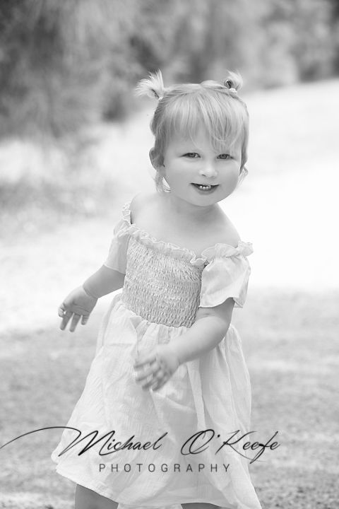 A series of black and white photos showing a small child in a white smocked dress playing outdoors.