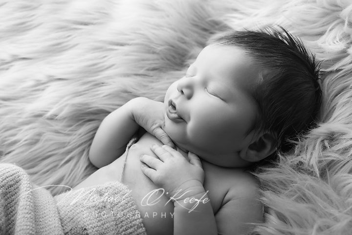 Black and white newborn photography of a sleeping baby smiling softly, lying on a fluffy fur blanket.