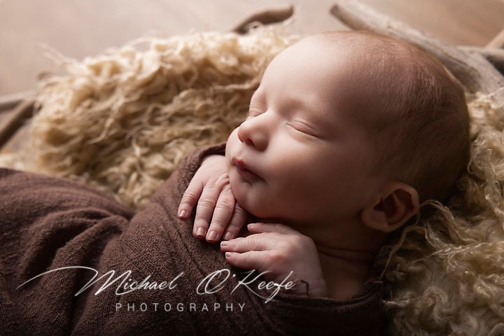 Newborn baby sleeping peacefully on soft beige blanket in professional photography studio setting.