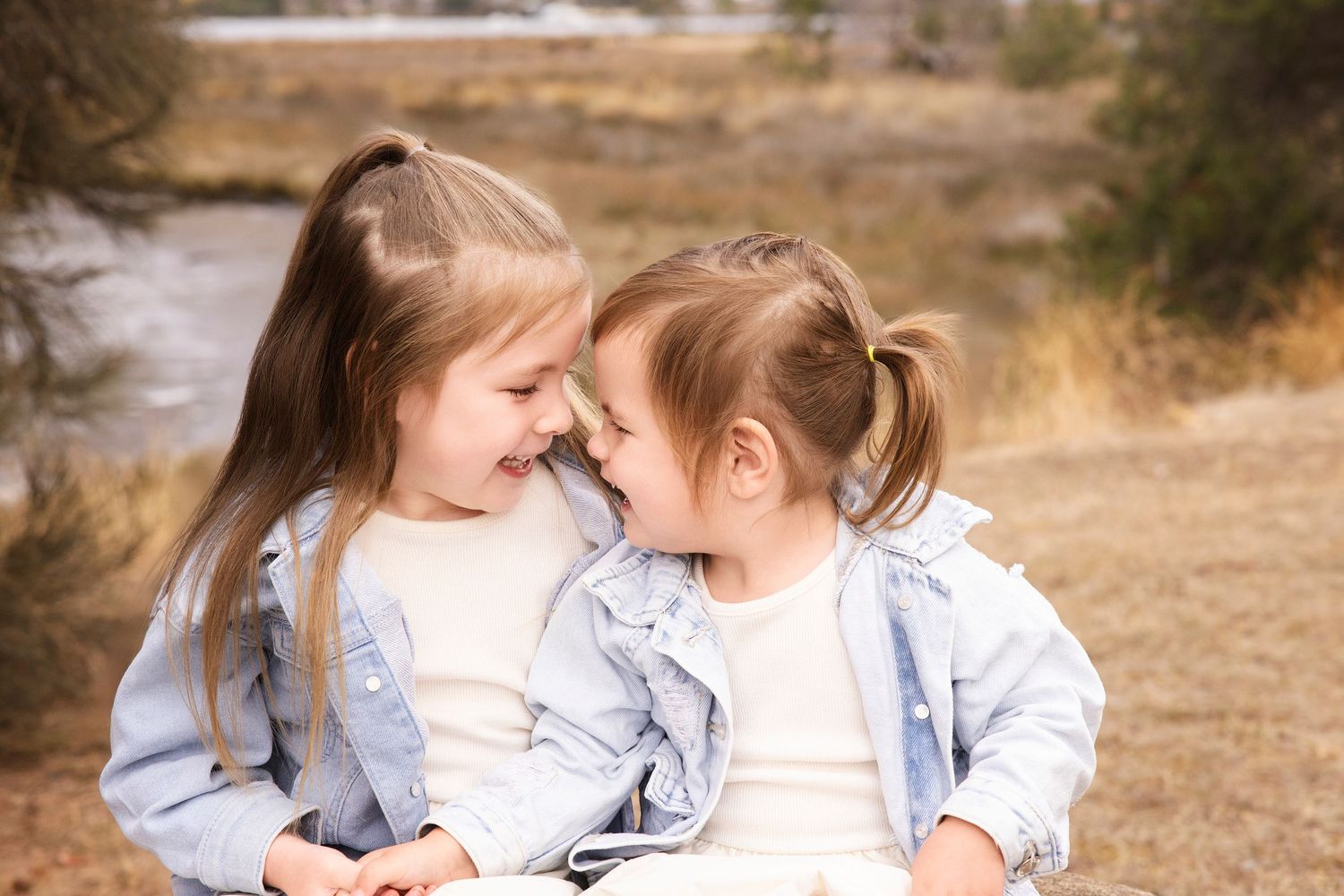 Two young girls in matching outfits sharing a laugh outdoors in natural setting.