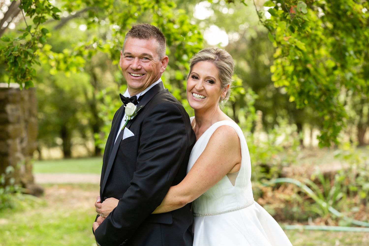 A bride and groom share a joyful moment together outdoors surrounded by lush greenery.