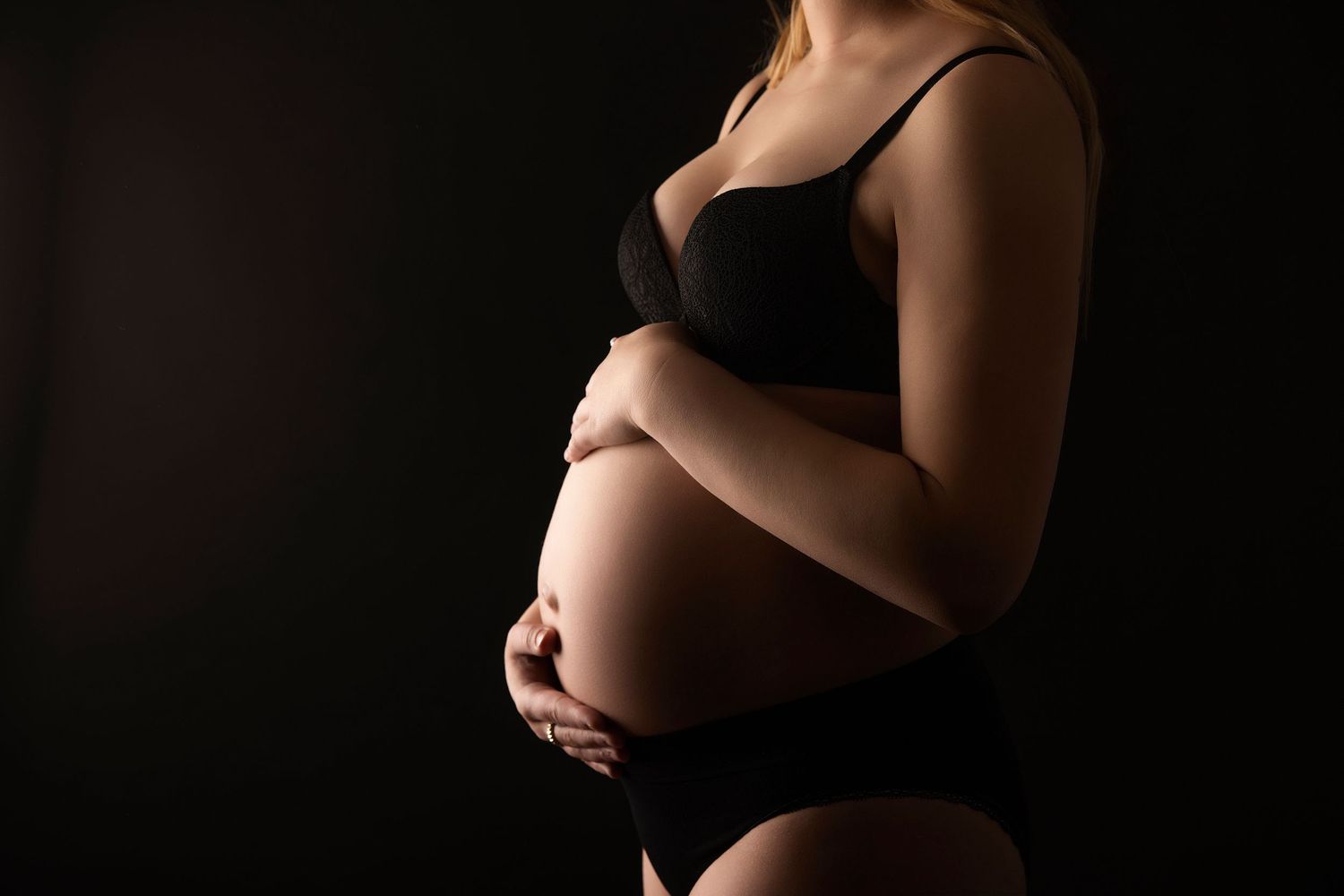 Side view maternity photo showcasing pregnant belly in intimate lighting against dark backdrop.
