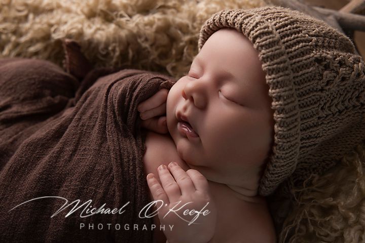 Peaceful newborn baby sleeping in brown knit bonnet and wrap on fluffy blanket, professional newborn photography.