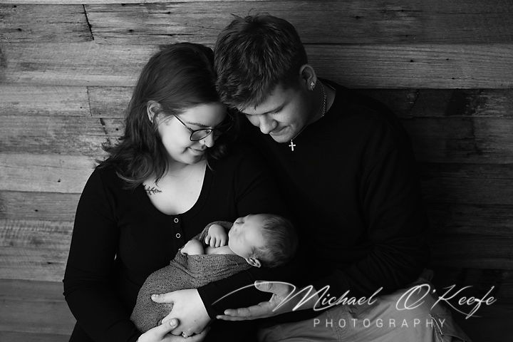 Intimate family moment with couple gazing at baby against wooden wall backdrop.