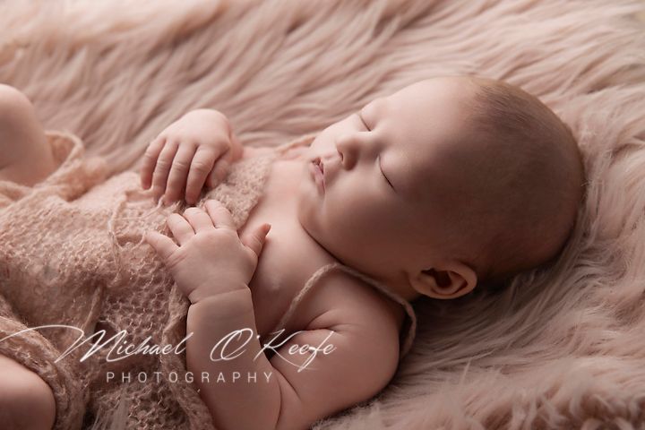 Sleeping baby on pink furry backdrop in natural light.