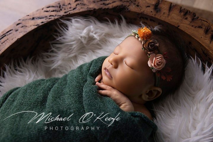 Artistic newborn photograph with floral accents on white fur backdrop.
