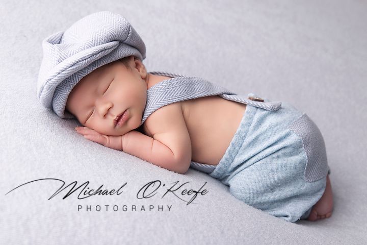 A sleeping baby in soft gray attire lies peacefully on a light backdrop in a professional newborn photography session.