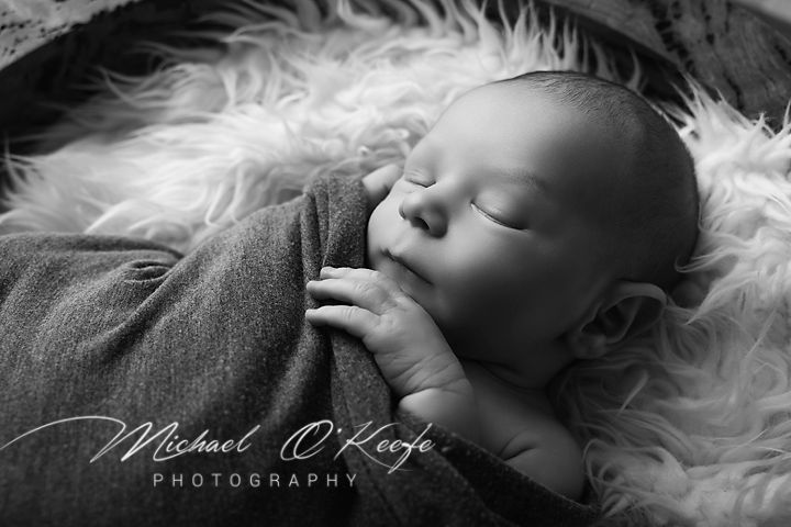 Black and white photograph of a sleeping infant resting peacefully on soft white fur bedding.
