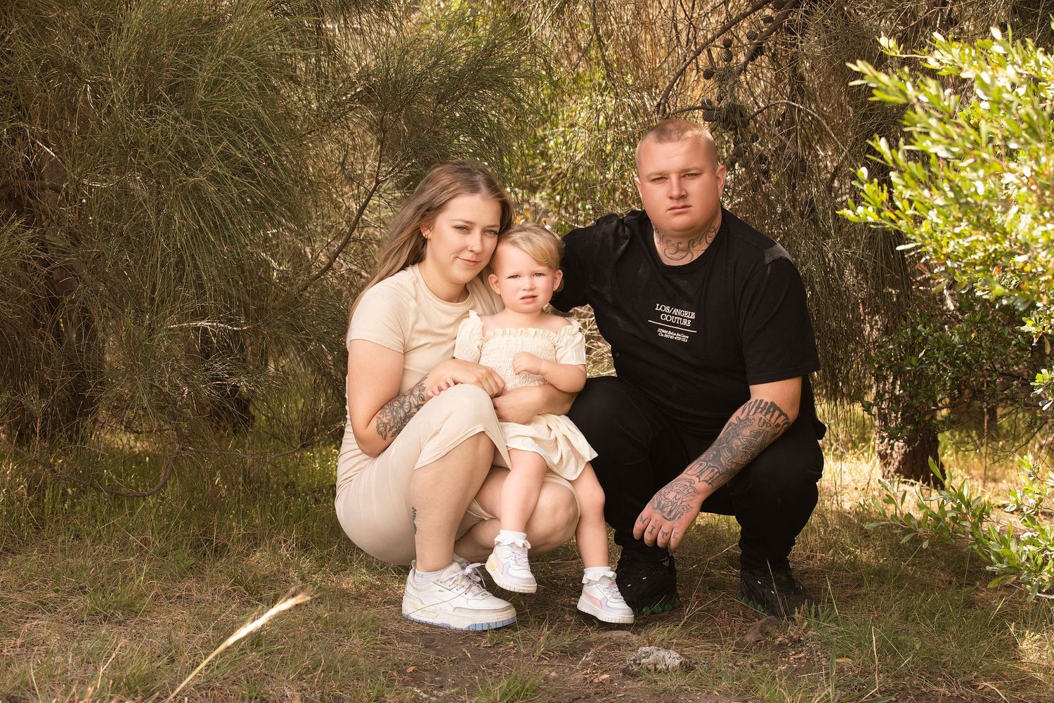 Family sitting together outdoors in casual clothing for a series of candid portrait photographs in natural lighting.