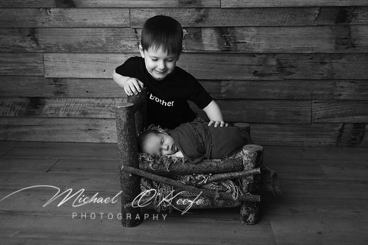 Black and white newborn photo of baby sibling with older brother smiling, by Michael O'Keefe Photography.