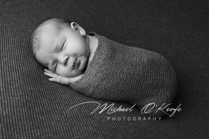 Black and white artistic newborn photography session featuring baby wrapped in soft gray fabric.