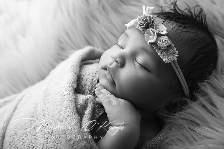 Black and white newborn photo of sleeping baby wrapped in knit blanket wearing floral headband.
