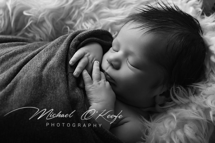 Black and white newborn portrait of sleeping baby wrapped in blanket by Michael O'Keefe Photography.