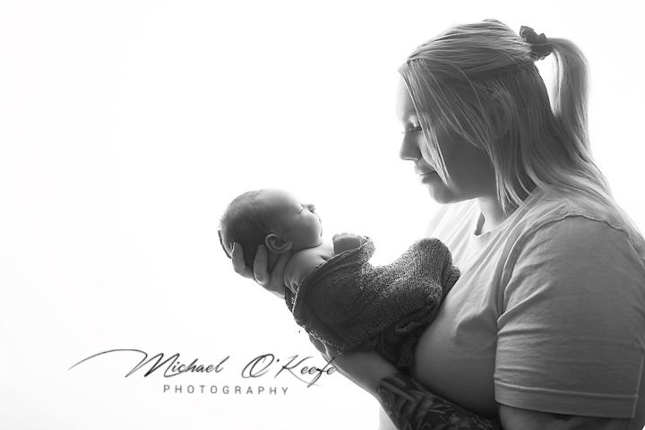Black and white portrait of a mother tenderly holding her newborn baby against a bright white background.