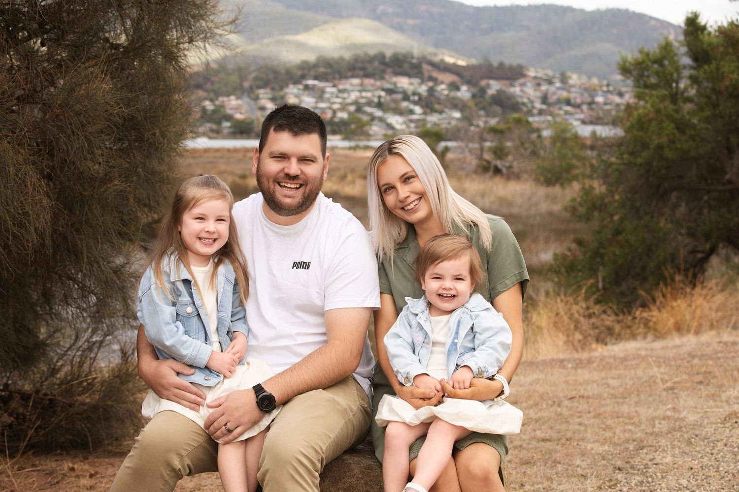 Family poses outdoors with mountains and suburban landscape in background.