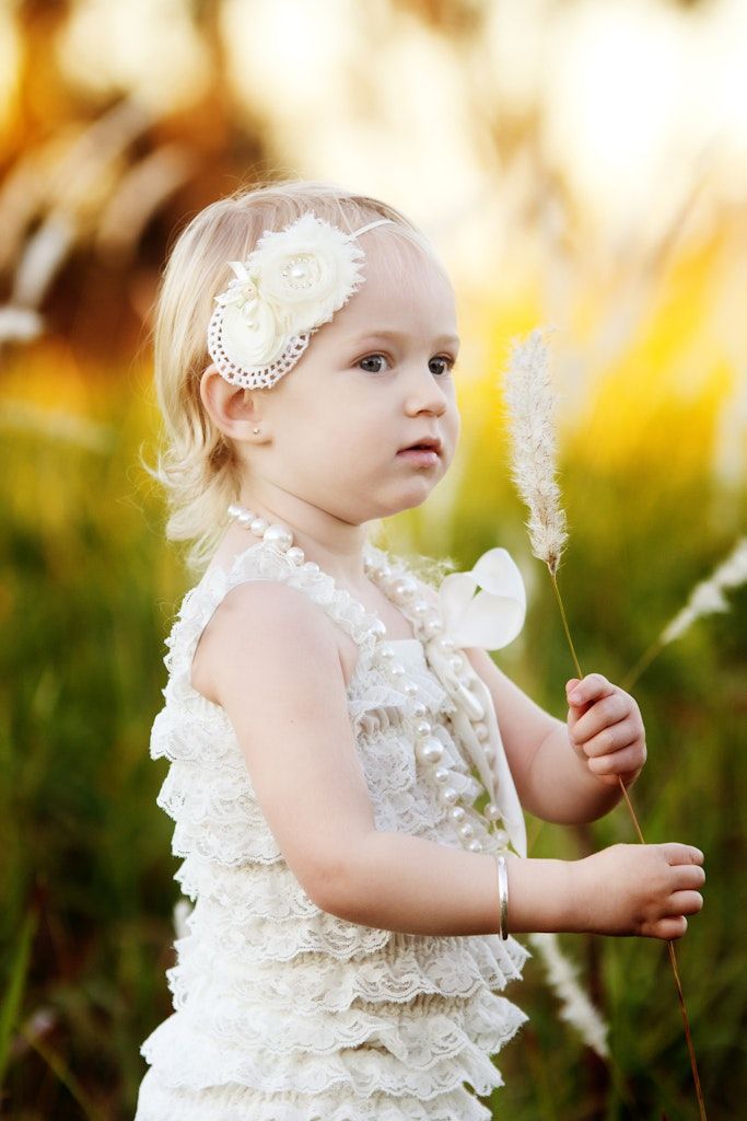 Little one in white lace dress and pearl headband exploring outdoors during golden hour.