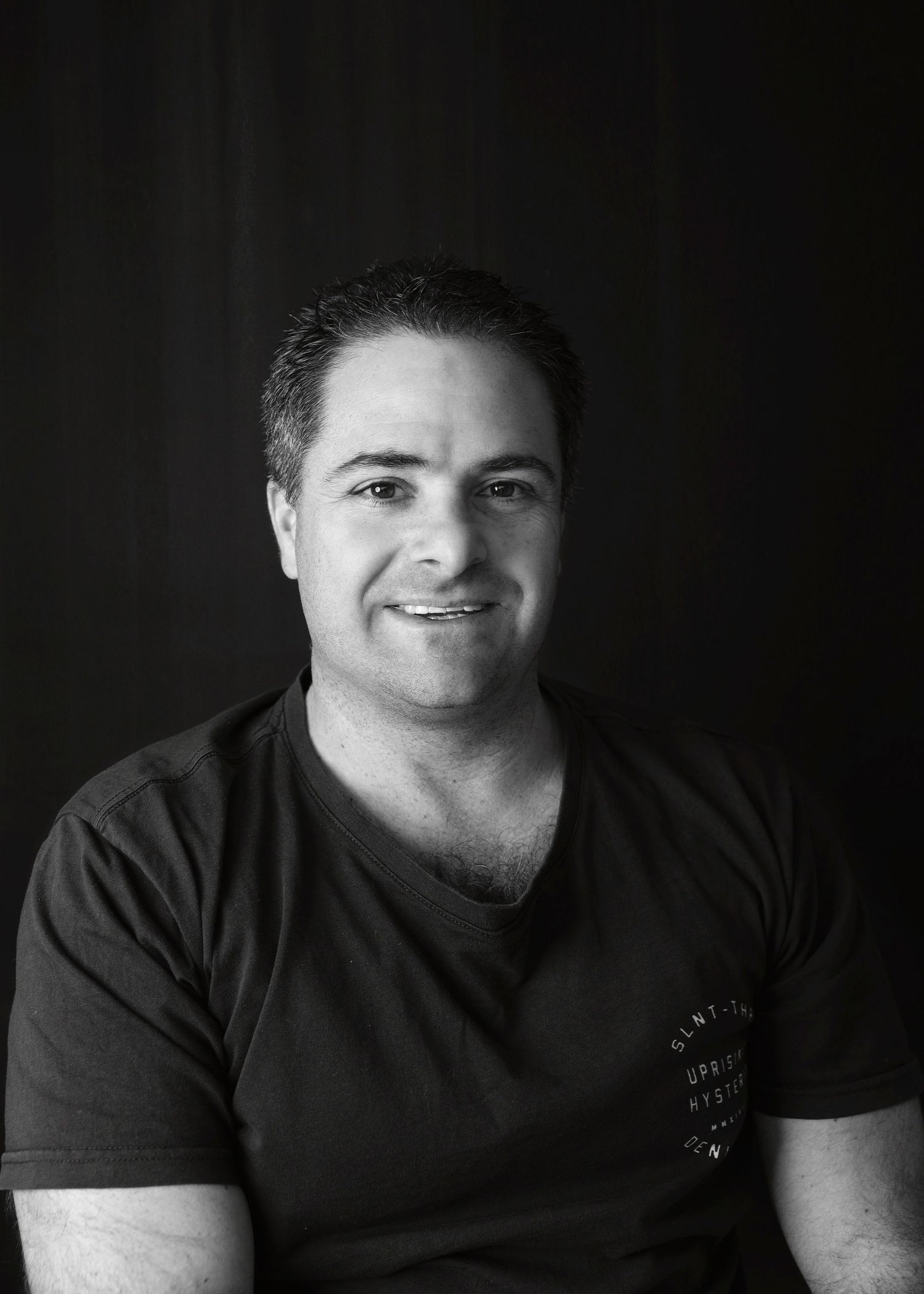 Professional black and white portrait of person in dark t-shirt against black background.