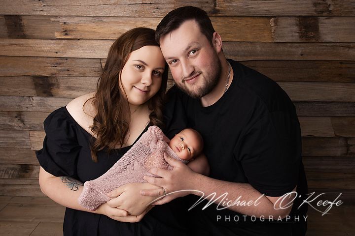 Romantic couple poses against rustic wooden wall backdrop in intimate engagement photo session.