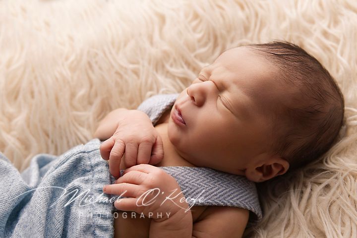 Sweet newborn baby sleeping peacefully on soft cream fur blanket while wearing cozy blue sweater.