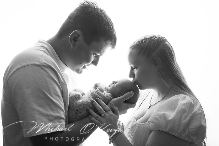 Black and white newborn photo of parents tenderly cradling their baby, captured by Michael O'Looney Photography.