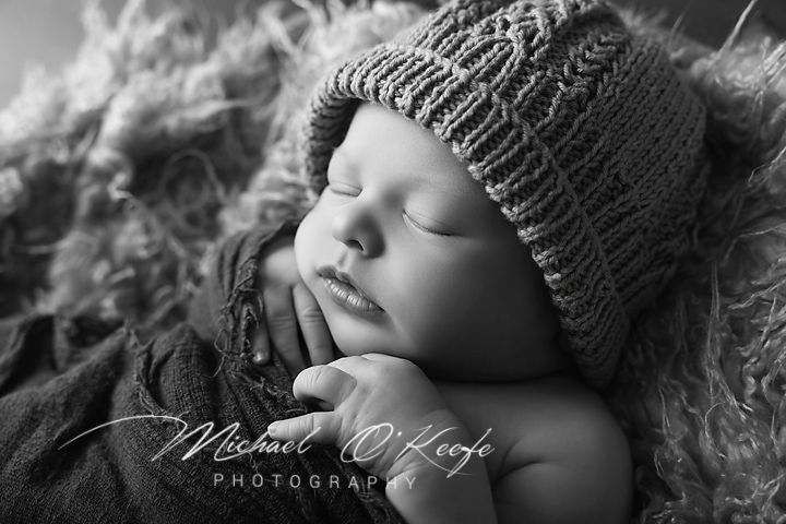 Black and white newborn photo of sleeping baby in knit hat, peaceful expression, by Michael O'Keeffe Photography.