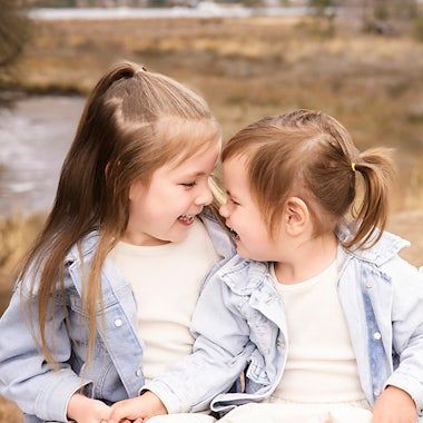 Two children sharing tender moments while wearing light blue outfits against a neutral background.