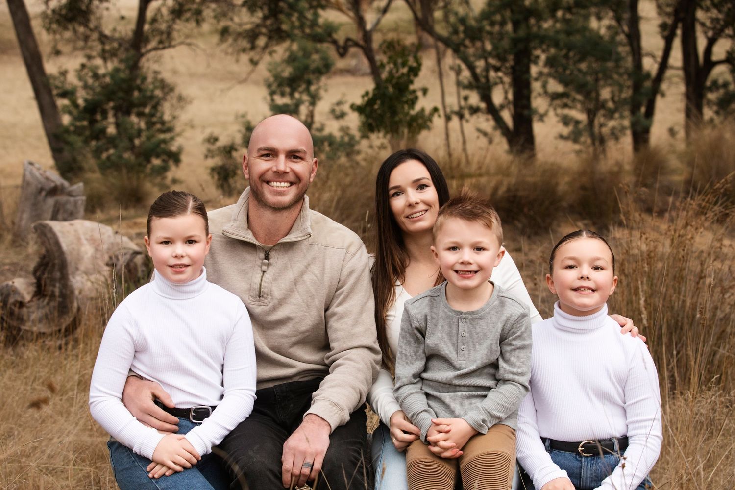 Family sits together on grassy hillside during casual outdoor photo session.