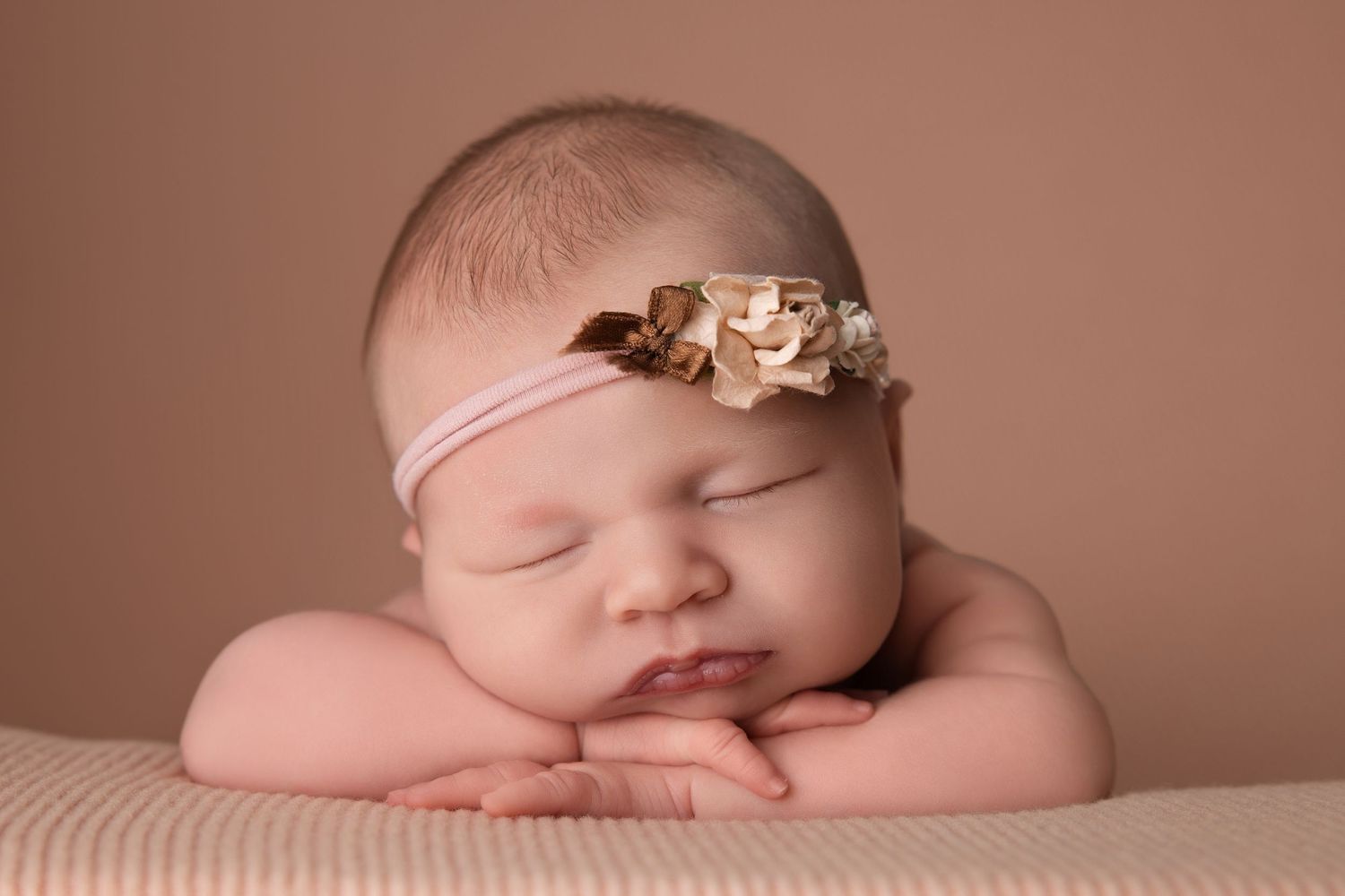 Peaceful sleeping baby with golden floral headband resting on folded arms.