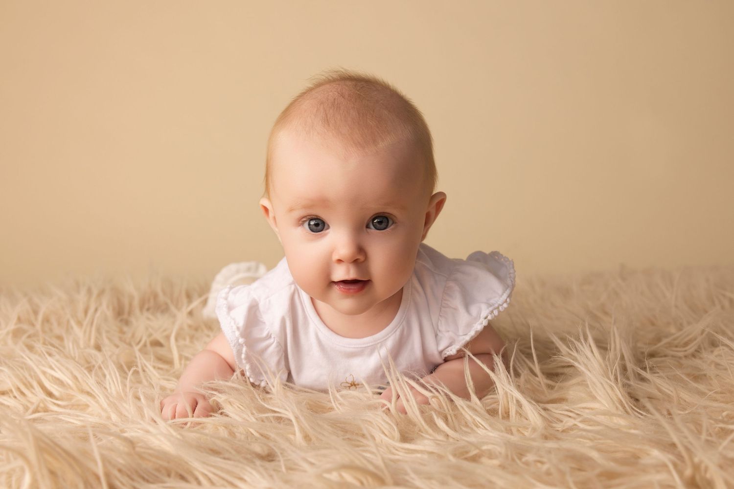 Smiling baby in white ruffled outfit on soft furry background.