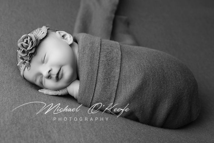 Black and white portrait of sleeping newborn with rose headband and wrap.