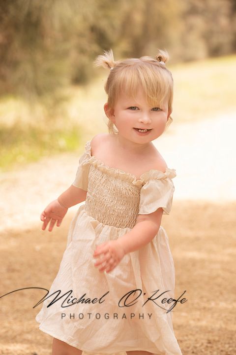 A toddler in a white flowing dress plays outdoors in warm sunlight creating a dreamy ethereal portrait series.