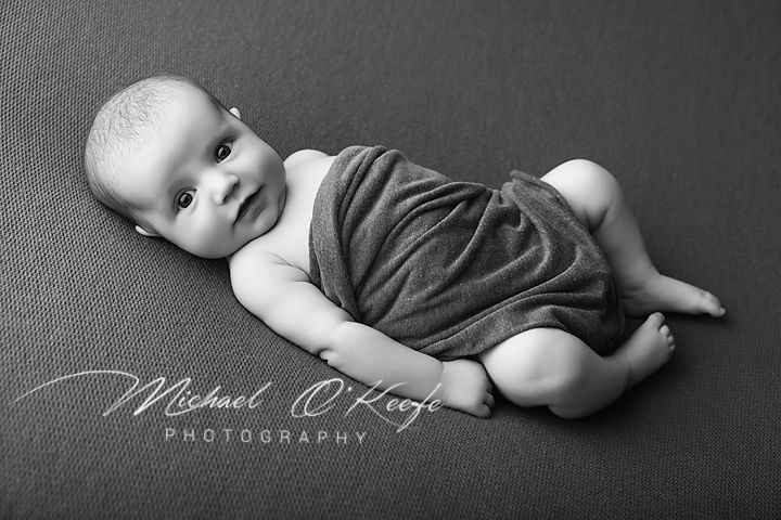 Black and white newborn photography of a swaddled baby lying on a soft blanket by Michael O'Keefe Photography.
