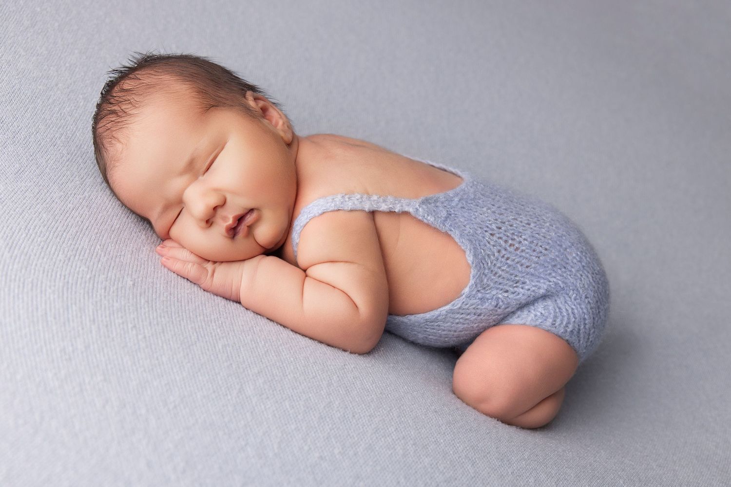 A series of soft, artistic newborn baby portraits in muted gray and blue tones showing peaceful sleeping poses.
