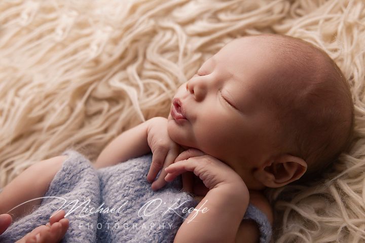 Newborn baby sleeping peacefully on soft cream-colored fur blanket in artistic black and white photography.